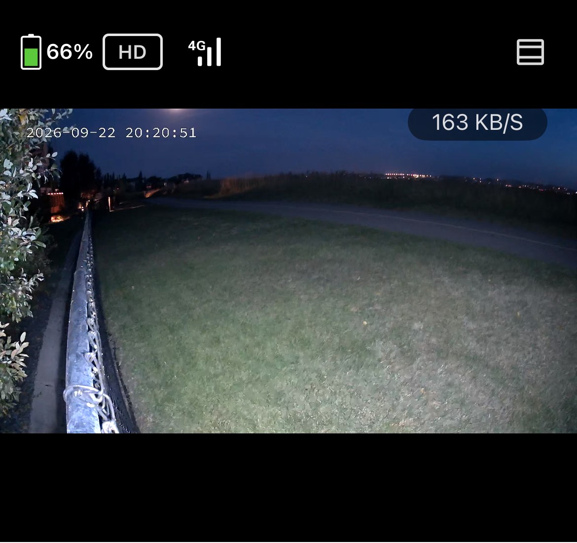 Color night vision footage with the built-in spotlight active, showing a yard in dusk-blue tones